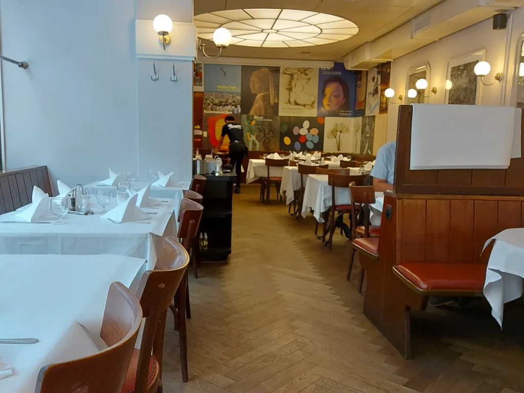 Inneneinrichtung des Aarbergerhof Bern: Weiss gedeckte Tische, Holzstühle und historische Poster an den Wänden.