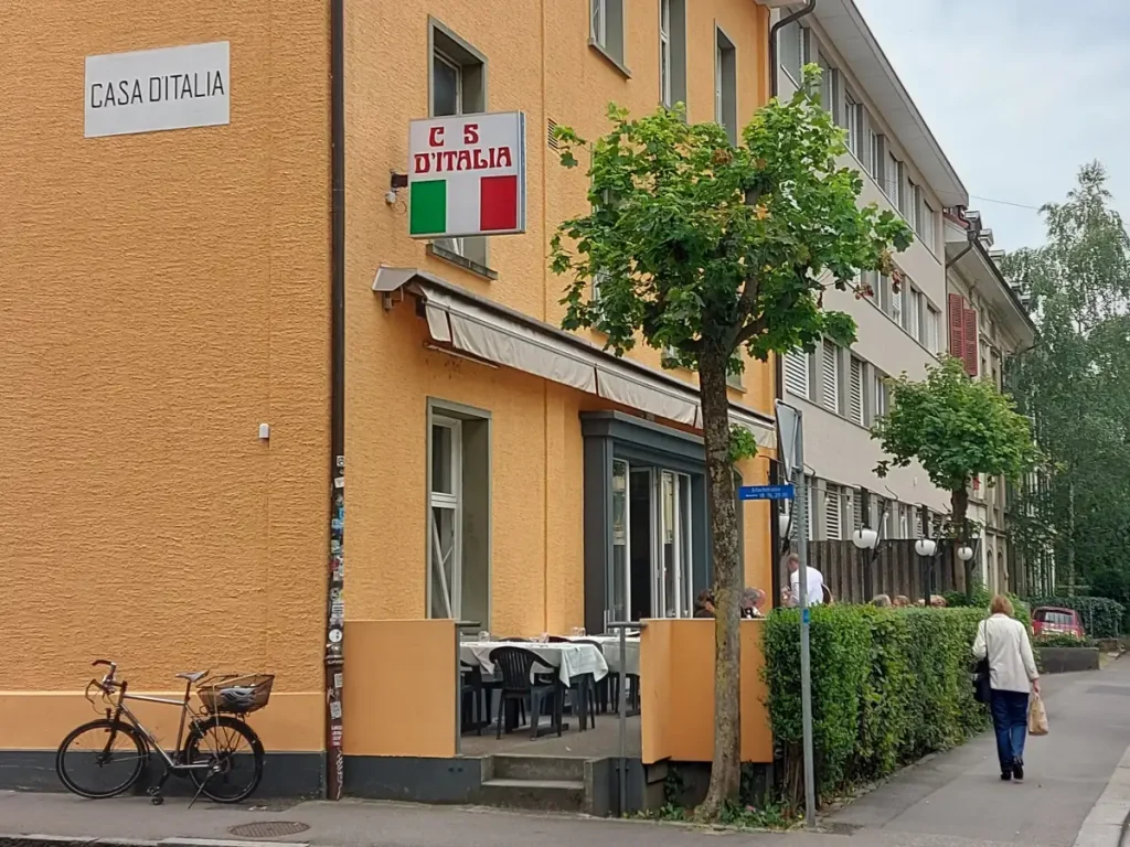 Casa d'Italia Bern: Einladende lachsfarbene Fassade mit ikonischem Schild und charmantem Fahrrad.