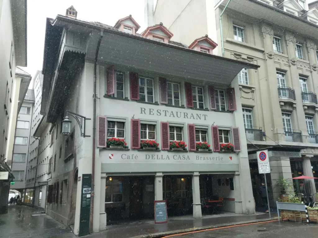 Historical building of Restaurant Della Casa Bern with red shutters and geraniums in the rain.