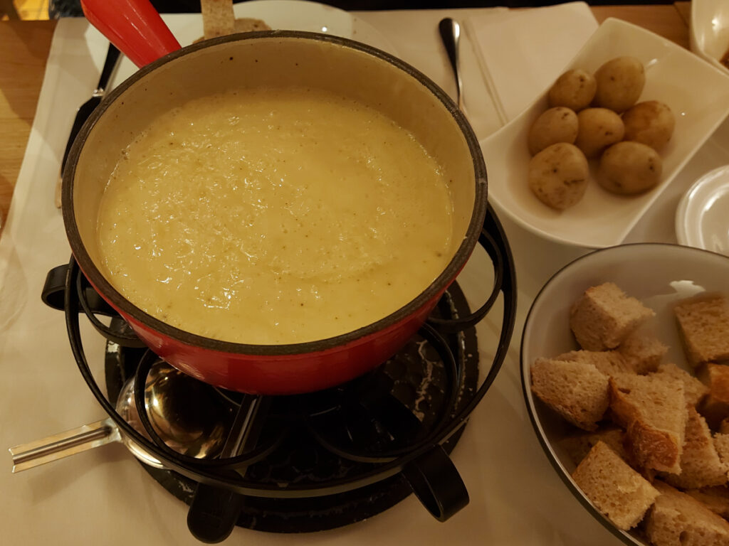 Creamy cheese fondue in a red caquelon on a rechaud, served with bread cubes and small potatoes (Gschwellti).