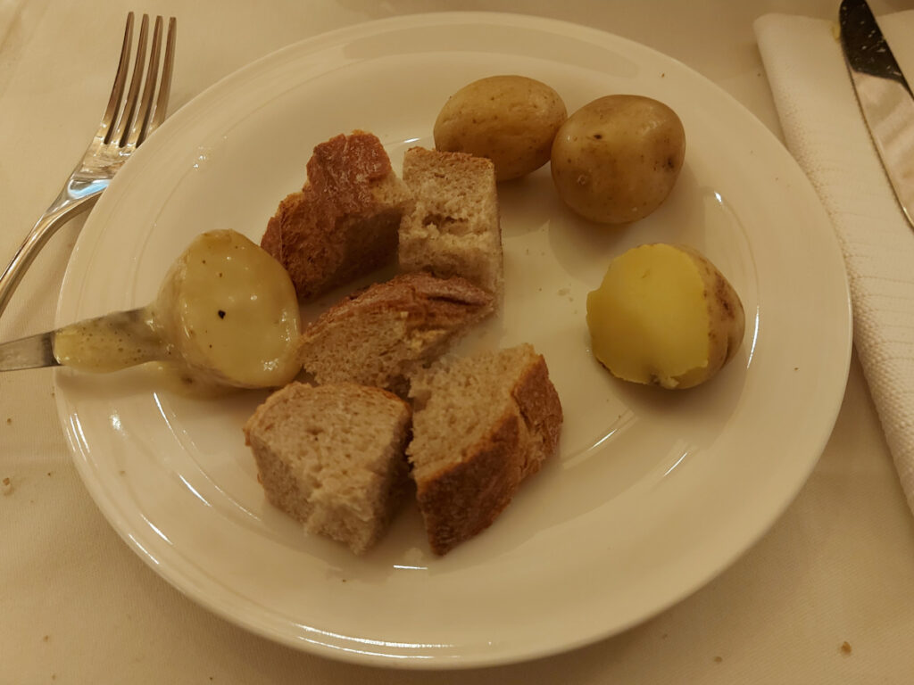 Close-up of a plate at Klötzlikeller Bern with bread cubes, Gschwellti, and a fondue fork with a potato covered in melted cheese.