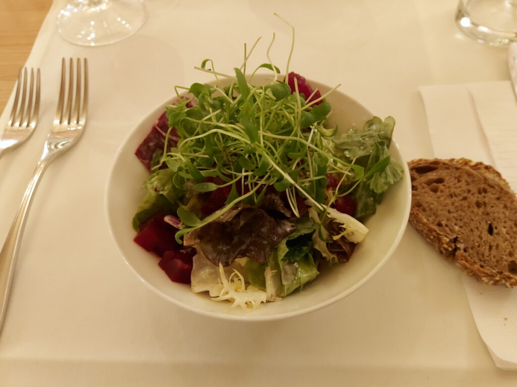 A small green leaf salad garnished with fresh cress in a white porcelain bowl.