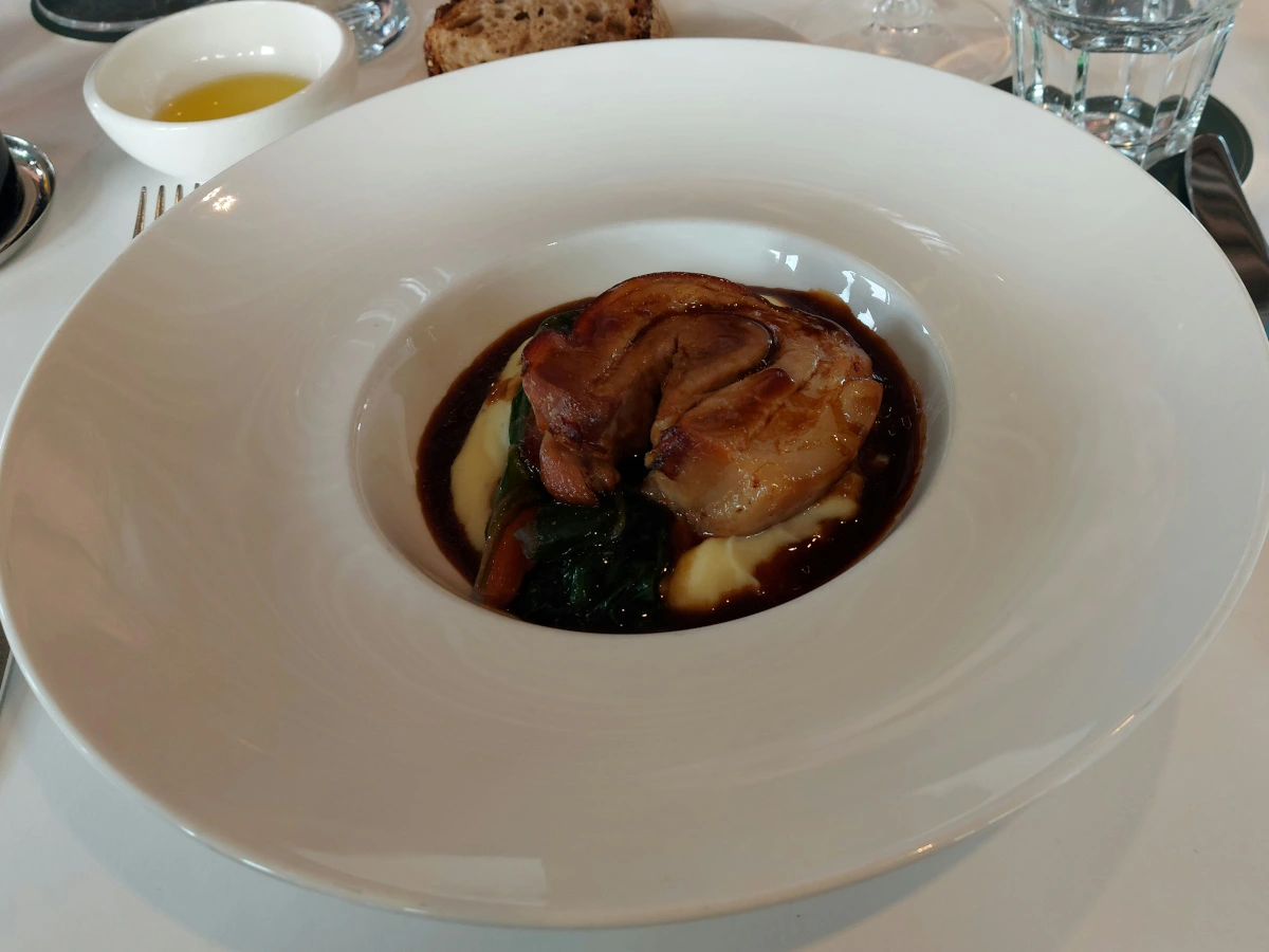 Eleganter Schweins-Rollbraten mit Rosmarin-Kartoffelpüree und dunklem Jus auf weissem Teller, serviert im Nido Bern.