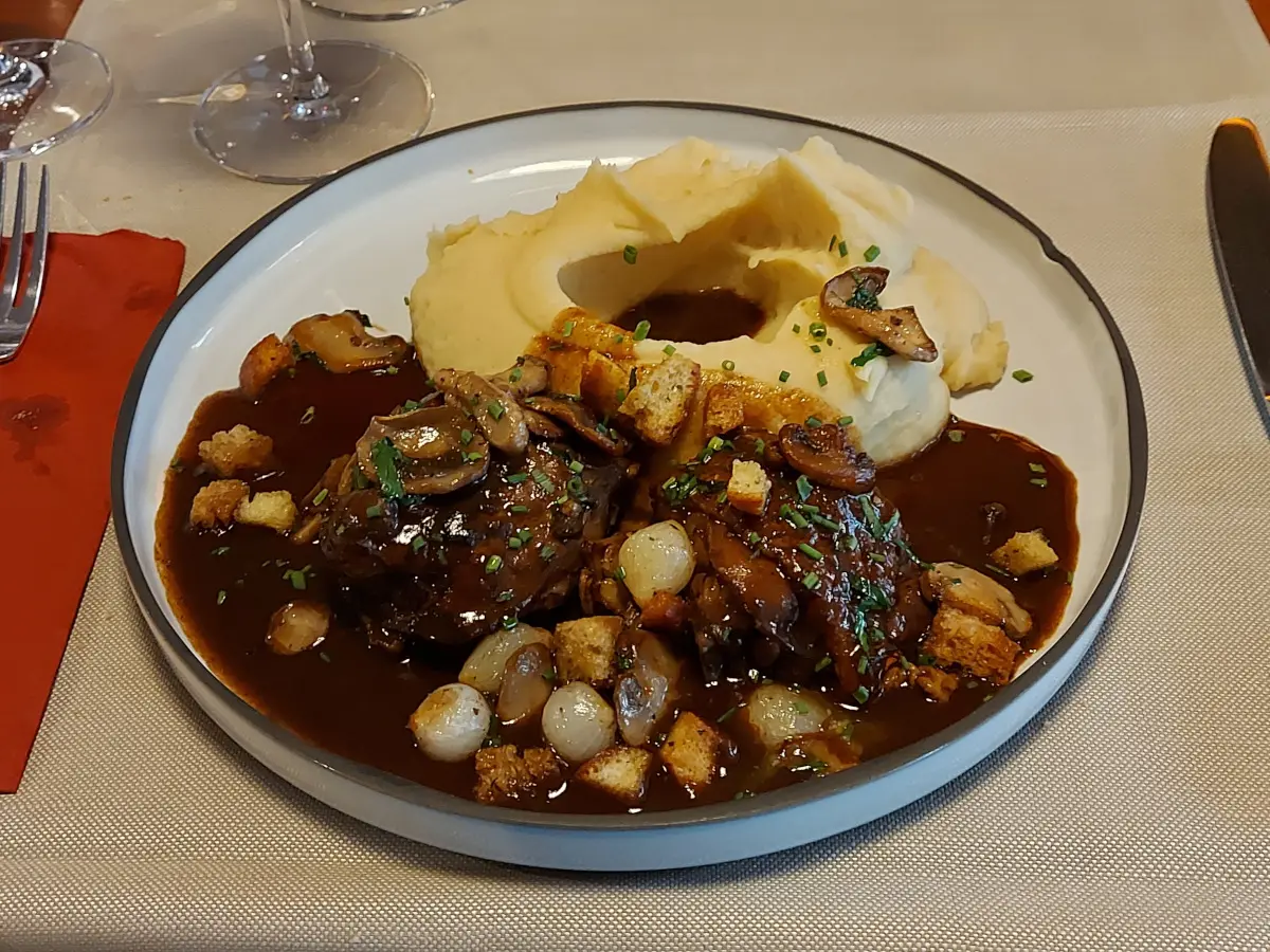 Coq au Vin im Ratskeller Bern: Zartes Hühnchen in kräftiger Rotweinsauce mit Pariser Zwiebeln, Champignons und cremigem Kartoffelpüree.