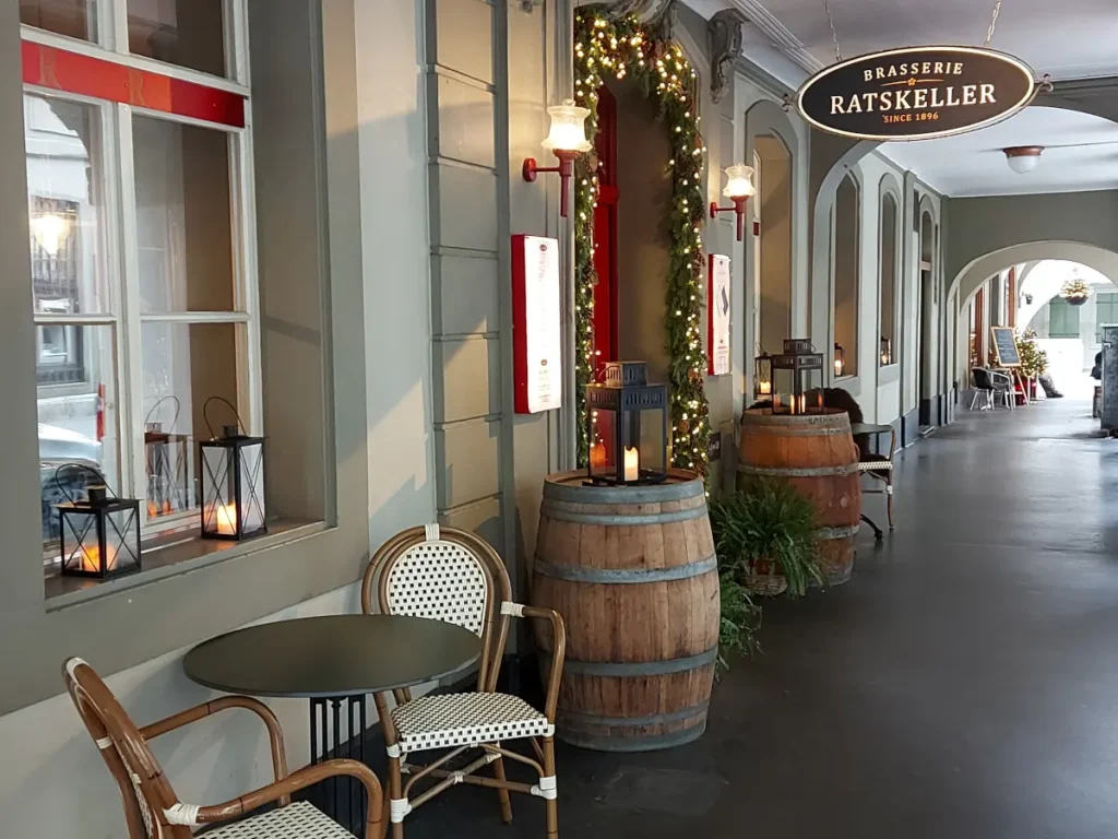 Entrance area of Ratskeller Bern: Wine barrels and small bistro tables under the arcade of an Old Town house.