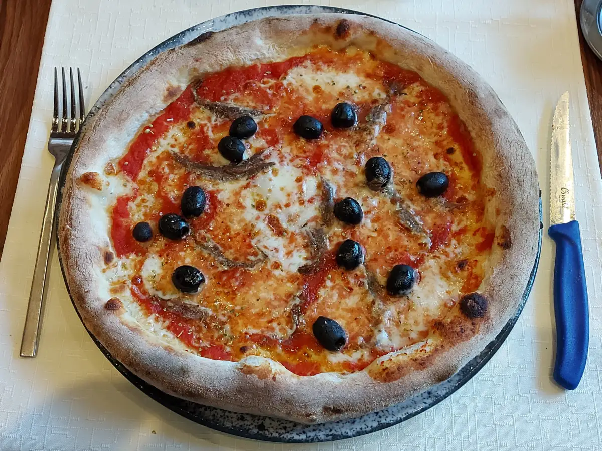Im Holzofen gebackene Pizza Napoletana vom Settebello Bern mit Tomatensauce, Mozzarella, schwarzen Oliven, Sardellen und unregelmäßig vom Feuer gebräunten Rändern.
