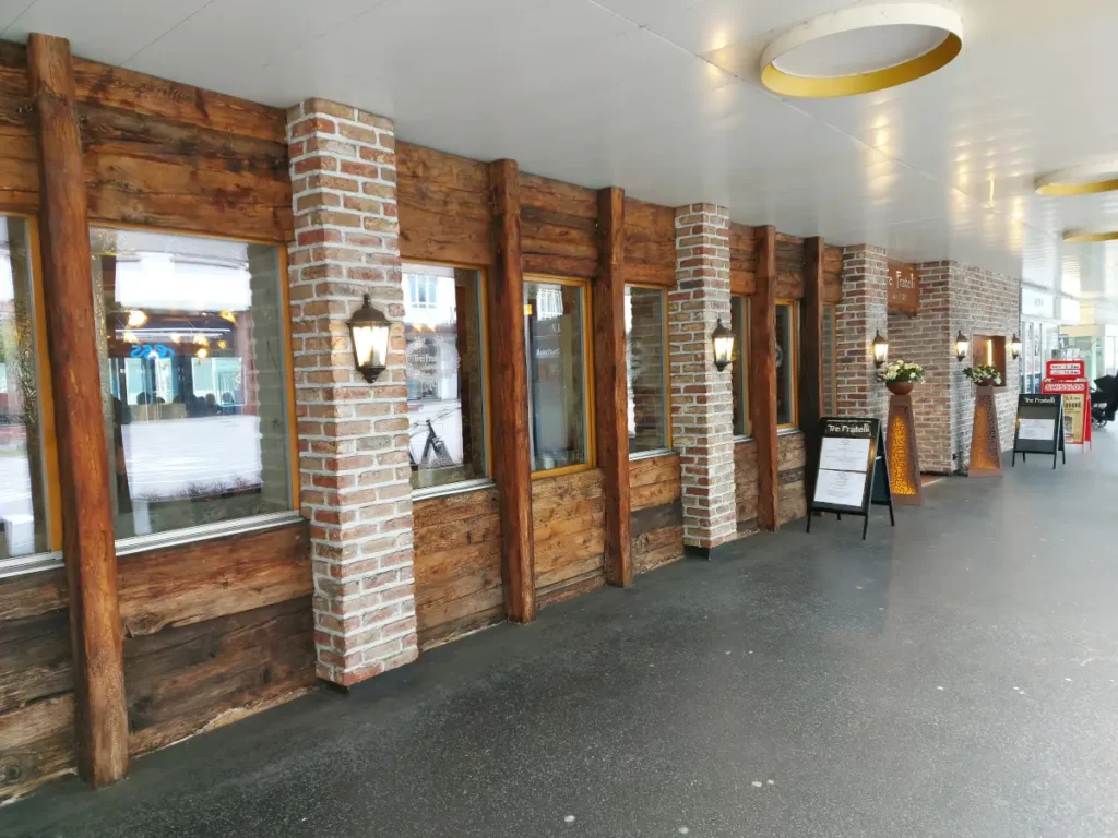 Aussenansicht des Restaurants Tre Fratelli in Bern mit Ziegelstein-Stützen und Holzdetails unter einer Laube.